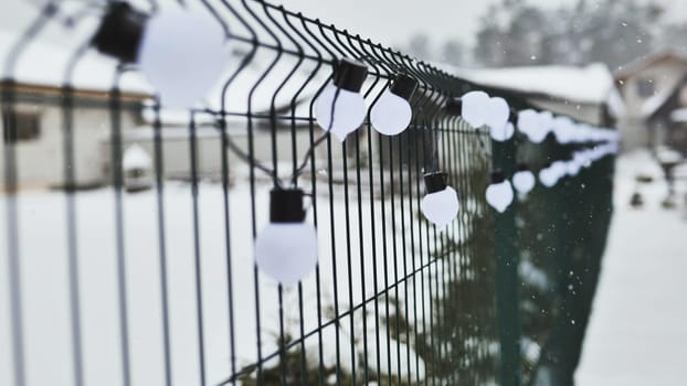 A white garland of bulbs on a fence in winter