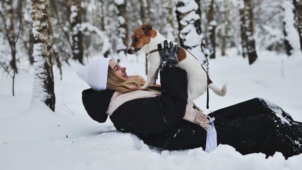 A girl falls in the snow with her Jack Russell Terrier dog in winter