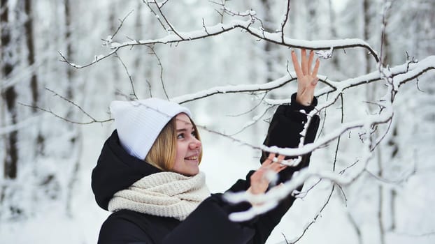A girl gently touches snowy tree branches in the forest