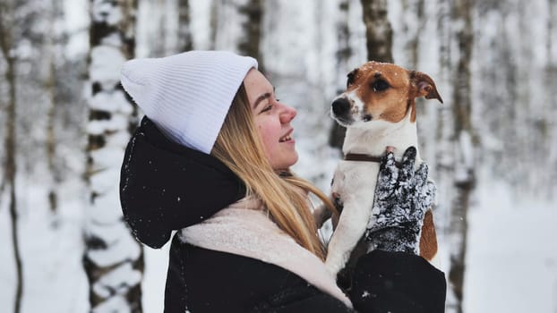 A girl kisses a Jack terrier dog in the winter woods