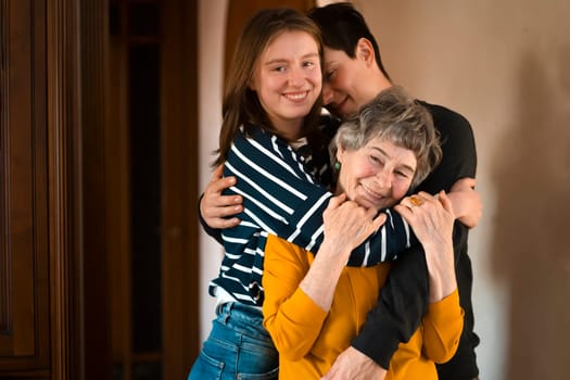 Young man and a girl happily hug their grandmother, the family lovingly takes care of their elderly parents and congratulates them on the holiday, the grandson with his sister visit an elderly woman.