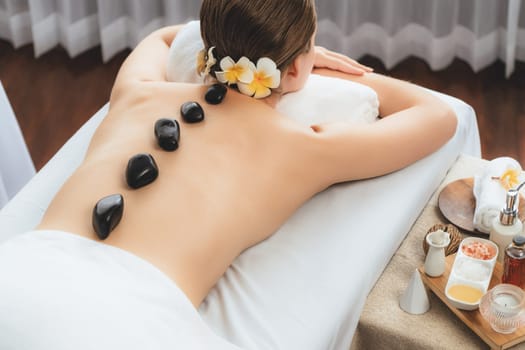 Hot stone massage at spa salon in luxury resort with day light serenity ambient, blissful woman customer enjoying spa basalt stone massage glide over body with soothing warmth. Quiescent