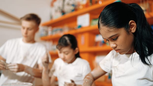 Smart teenager modeling cup of clay while laughing at art lesson. Diverse happy student standing while doing creative activity at workshop. Creative activity concept. Blurred background. Edification.