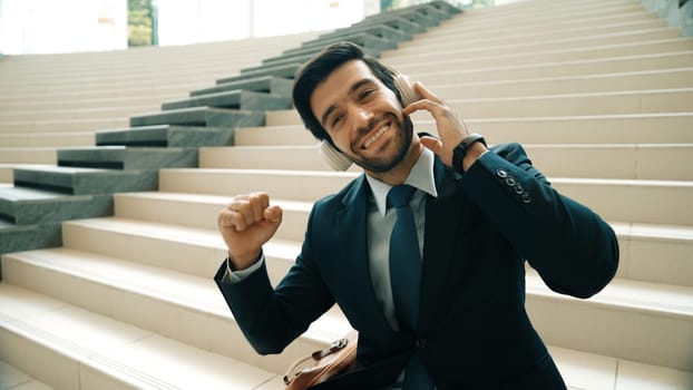 Closeup image of professional business man enjoy to listen music by using headphone. Portrait of skilled project manager show facial expression about joy and happy while sitting at mall. Exultant.