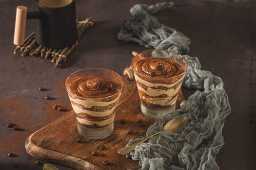 Delicious italian dessert tiramisu in a glasses on a dark slate, stone or concrete background.