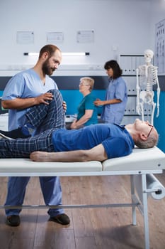 Physiotherapist is assisting elderly man recovering from a leg injury. Senior patient receiving help from a chiropractor for knee discomfort and muscular tightness to aid in rehabilitation.