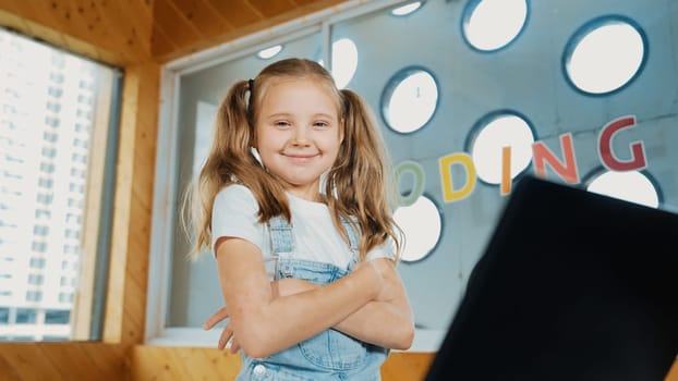 Girl using laptop programing software while looking at camera with arm folded with confident to celebrate successful project. Pretty child coding system while crossing arms in Stem class. Erudition.