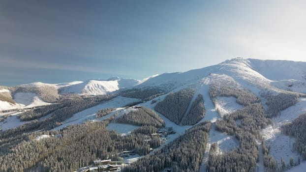 Aerial winter view of Demanovska Dolina village in Low Tatras mountains, Slovakia. Drone panoramic view to ski resort houses among coniferous forest in snow and ice, snowy cable car station at sunset