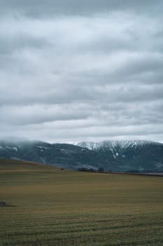 Scenic landscape of Low Tatras mountains, farmland field and cloudy foggy sky in Slovakia