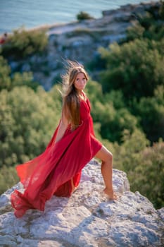 Woman sunset sea red dress, back view a happy beautiful sensual woman in a red long dress posing on a rock high above the sea on sunset