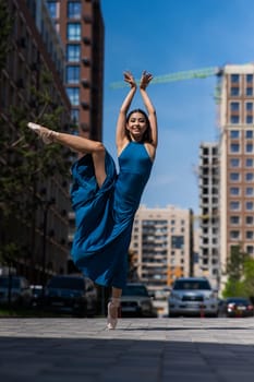 Beautiful Asian ballerina in blue dress posing in splits outdoors. Urban landscape. Vertical photo