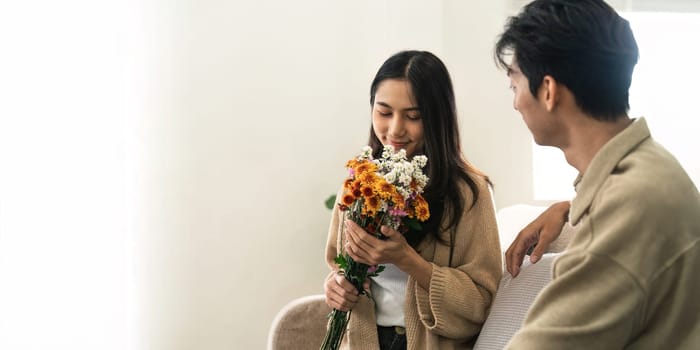 Asian handsome man show the love and give flowers to his girlfriend in living room on valentine day. Lifestyle Concept.