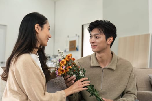 Asian handsome man show the love and give flowers to his girlfriend in living room on valentine day. Lifestyle Concept.