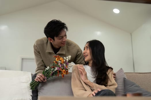 Asian handsome man show the love and give flowers to his girlfriend in living room on valentine day. Lifestyle Concept.