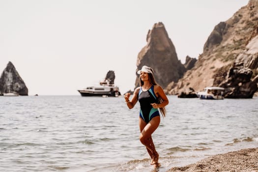 Woman beach vacation photo. A happy tourist in a blue bikini enjoying the scenic view of the sea and volcanic mountains while taking pictures to capture the memories of her travel adventure