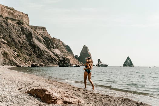 Woman beach vacation photo. A happy tourist in a blue bikini enjoying the scenic view of the sea and volcanic mountains while taking pictures to capture the memories of her travel adventure