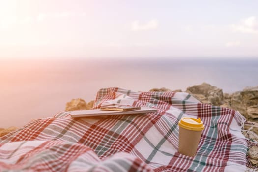 Laptop coffee on blanket with ocean view. Illustrating serene outdoor laptop use. Freelancer enjoying their time outdoors while working or browsing the internet