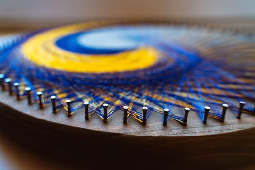 Colored thread mandala on a wooden board with nails. Mandala Moon Harmony Sun esotericism and psychology pictures from yellow and blue silk threads