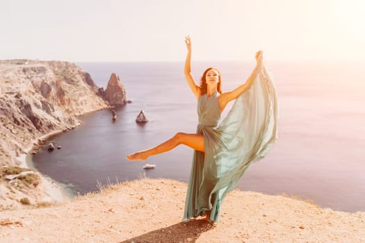 Woman green dress sea. Female dancer posing on a rocky outcrop high above the sea. Girl on the nature on blue sky background. Fashion photo