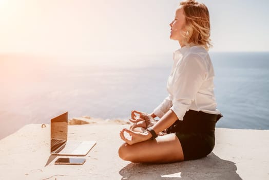 Happy girl doing yoga with laptop working at the beach. beautiful and calm business woman sitting with a laptop in a summer cafe in the lotus position meditating and relaxing. freelance girl remote work beach paradise