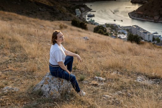 Happy woman on sunset in mountains. Woman siting with her back on the sunset in nature in summer. Silhouette