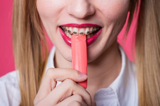 Portrait of a young woman with braces and bright makeup chewing gum on a pink background