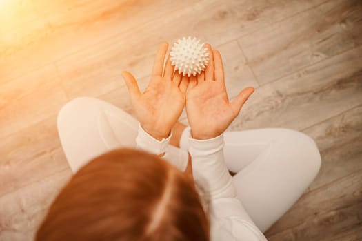 Athletic slim caucasian woman doing thigh self-massage with a massage ball indoors. Self-isolating massage.