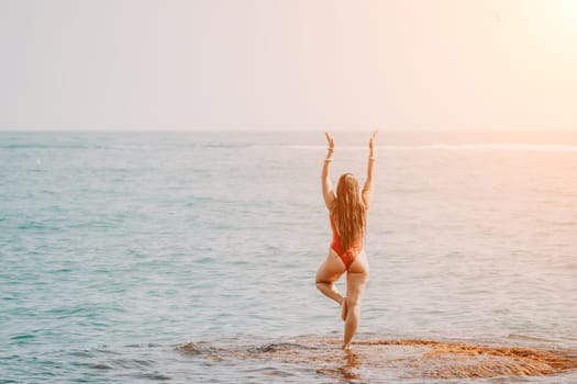 Woman sea yoga. Back view of free calm happy satisfied woman with long hair standing on top rock with yoga position against of sky by the sea. Healthy lifestyle outdoors in nature, fitness concept.