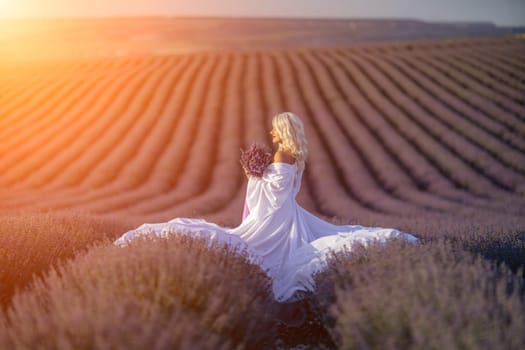 Blonde woman poses in lavender field at sunset. Happy woman in white dress holds lavender bouquet. Aromatherapy concept, lavender oil, photo session in lavender.