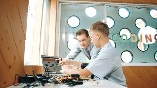 Smart student present coding program and car model to skilled teacher. Teenager using computer to programing system for robotic machines at table with electronic equipment scatter around. Edification.