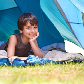 Boy, child and camping, relax in tent and summer vacation with travel and happy in portrait outdoor. Rest on sleeping bag, young camper with smile and adventure in nature, childhood and recreation.