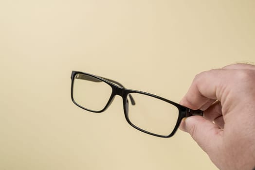 Hand holding black framed prescription glasses in front of yellow background