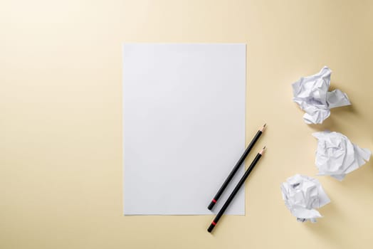 Blank writing sheet with pen and crumpled paper balls lay flat on yellow background