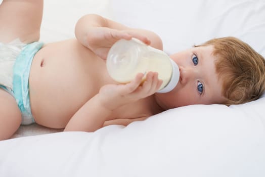 Portrait, bottle and baby in bed drinking milk for meal, feeding or food lying down in home. Hungry child, wellness and healthy boy toddler with formula for nutrition, natural diet or growth alone.