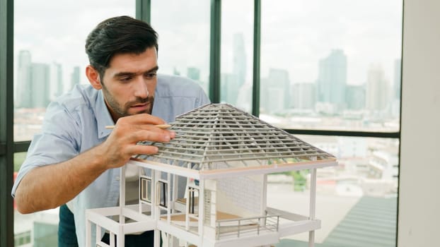Professional architect engineer using pencil measuring model roof length at modern office with skyscraper, cityscape view. Skilled project manger or businessman check house construction. Tracery