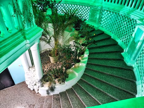 Snail stone staircase with steps, white railings, green flowers and plants inside. Architecture. Abstract Background, location and pattern