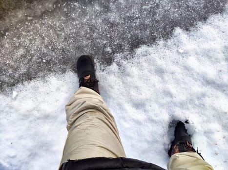 Feet of Hunter or fisherman in big warm boots on winter day on snow. Top view. Fisherman on the ice of a river, lake, reservoir on spring day with melting ice. Dangerous fishing in autumn