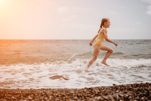 Cute little girl running along the seashore against a clear blue sea and rejoices in the rays of the summer sun. Beautiful girl in yellow swimsuit running and having fun on tropical beach