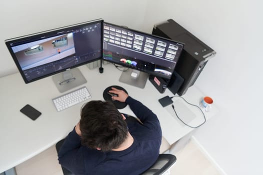 professional video editor enhancing digital footage using specialized software. Expert videographer in home office workspace editing on dual screen workstation computer desktop workplace