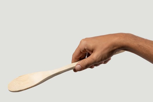 Black male hand holding a wooden cooking spoon on grey background. High quality photo