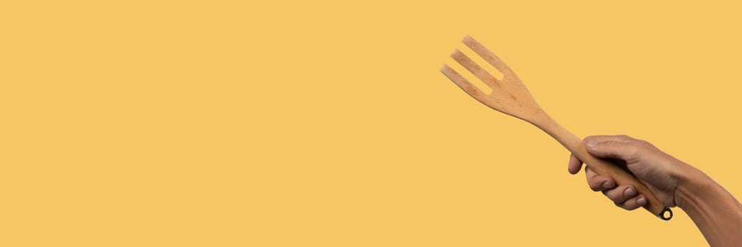 Hand holding wooden fork yellow background banner cutout. High quality photo