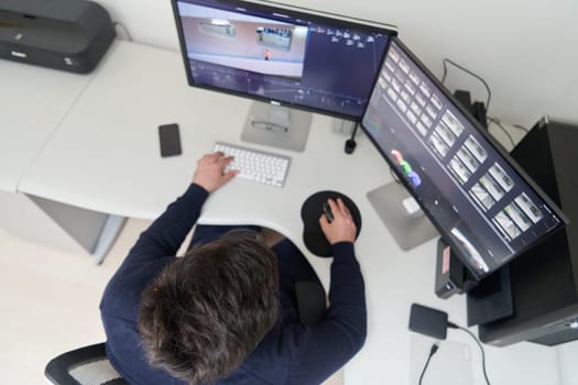 professional video editor enhancing digital footage using specialized software. Expert videographer in home office workspace editing on dual screen workstation computer desktop workplace