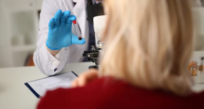 Doctor holds analyzed blood sample front patient. Laboratory studies under microscope. Test tubes in laboratory. Sanitary station. Sample for detection on coronavirus. Woman waiting for test result