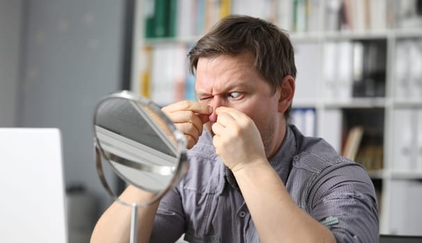 Man at home squeezes fingers acne in front mirror. Skin rashes. Person concentrates on acne during self-isolation. Improve skin condition yourself. Spending free time in apartment during quarantine