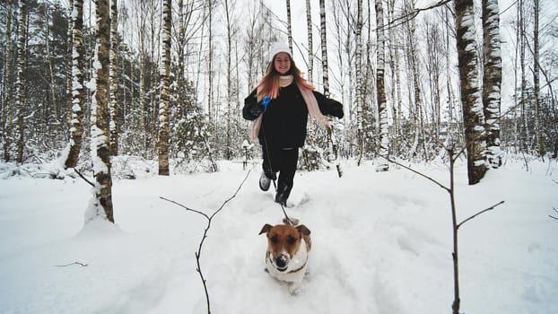 A girl and her Jack Russell Terrier dog are running through the woods