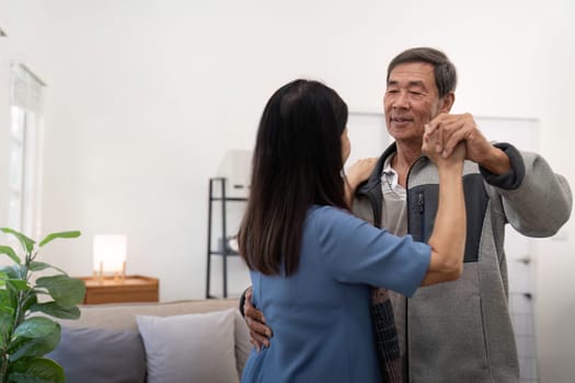 Elderly couple in love looking at each other with tenderness while dancing together in living room at home.
