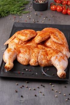 Whole chicken carcass with seasonings on on a black platter for your meat menu or booklet design.