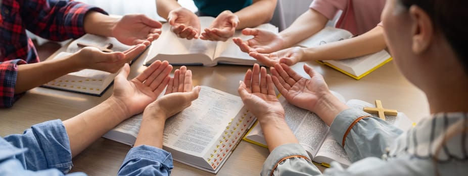 Cropped image of diversity people hand praying together at wooden church on bible book. Group of believer hold hand together faithfully. Concept of hope, religion, faith, god blessing. Burgeoning.