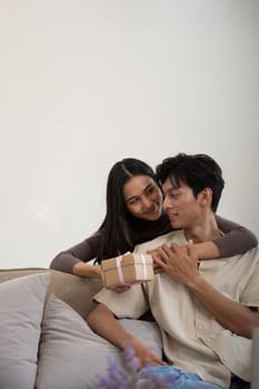 Romantic young asian couple embracing giving present in living room at home. Fall in love. Valentine concept. Surprise gift.