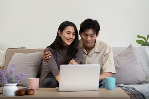 Young couple asian using laptop together while sitting on sofa at home.